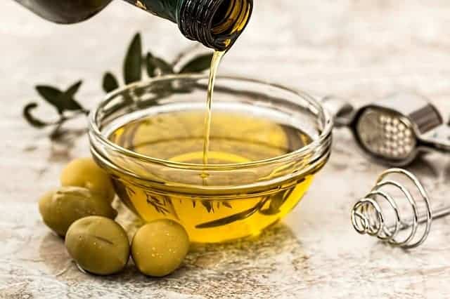 huile versée dans un bol, olives vertes à côté