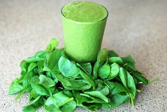 Un verre avec un smoothie vert, des feuilles d'épinards tout autour
