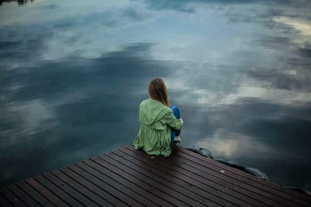  une femme est assise sur le bord d'une jetée et regarde l'eau.