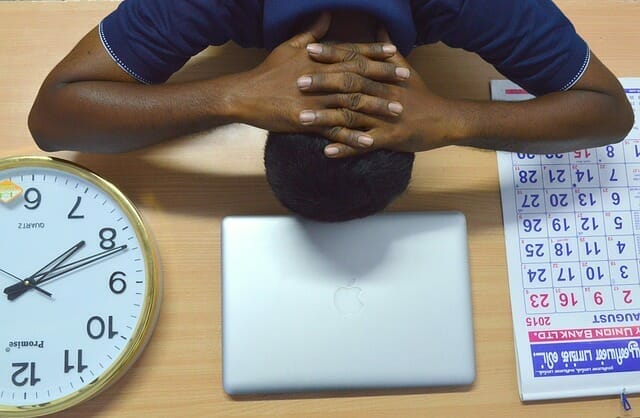  Un homme fatigué pose sa tête sur son bureau, à côté de son ordinateur portable, de son calendrier et de son horloge.